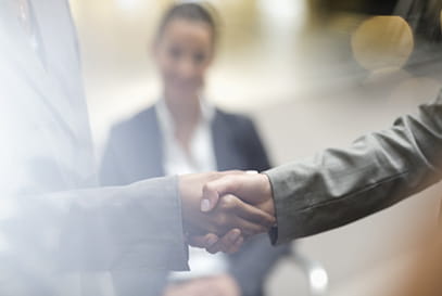 Young woman watches as two businesspeople shake hands